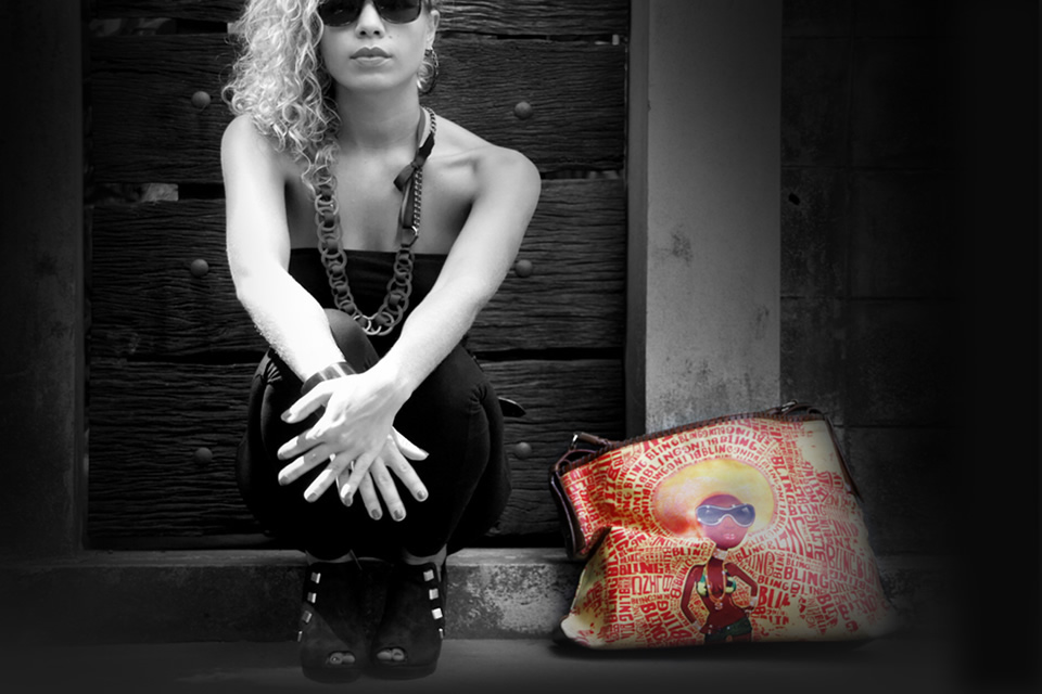 Tookata campaign photograph: a woman in black crouches beside a brightly illustrated Tookata bag, the only colour in the black-and-white frame